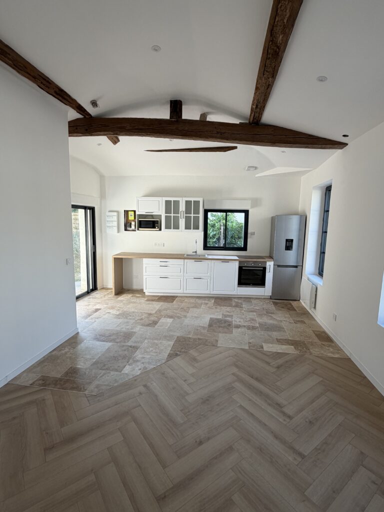 Pièce de vie rénovée avec cuisine, poutres apparentes et parquet chevron
